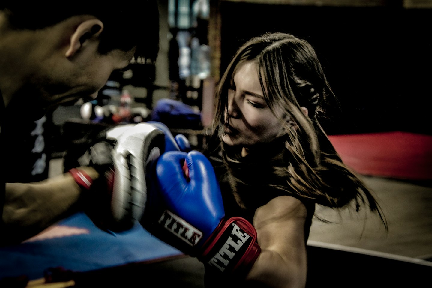 Woman in blue gloves punches a training mitt held by instructor.