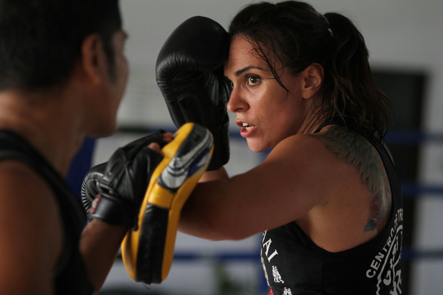 Woman in black boxing gloves training with focus mitts.