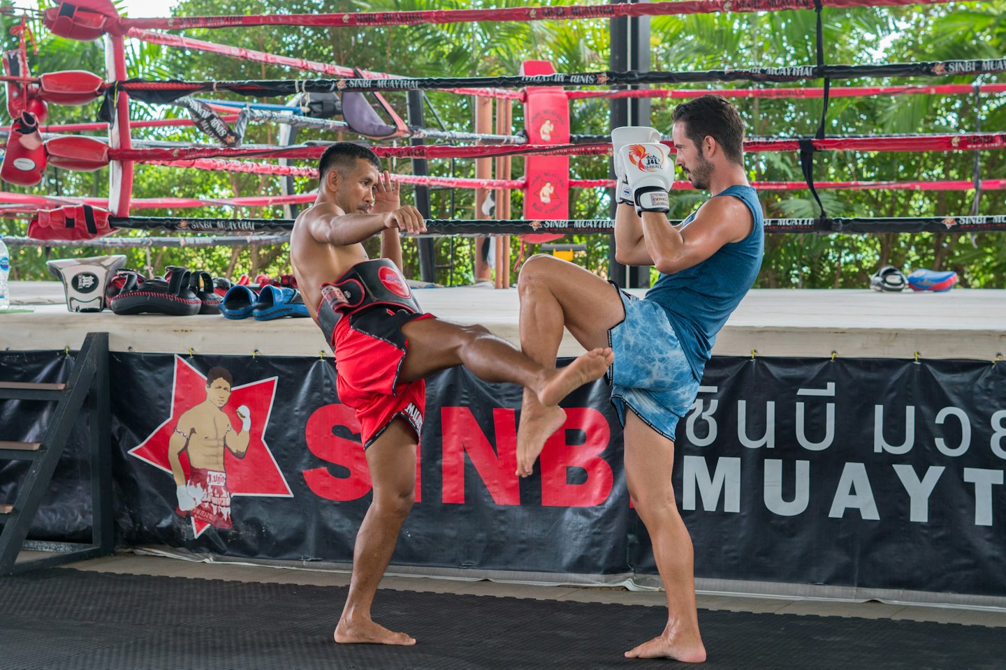 Two boxers practice Muay Thai inside an outdoor ring.